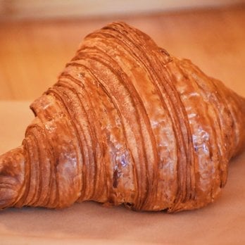 Golden brown croissant with flaky, layered pastry on a warm orange background