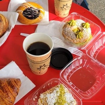 Assorted pastries and desserts on red trays with coffee cup and pistachio-topped treats on a red table