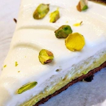 Slice of pistachio dessert with white frosting, pistachio garnish, and layered cake base