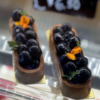 Two chocolate éclairs topped with fresh blueberries and yellow flowers on a display platter