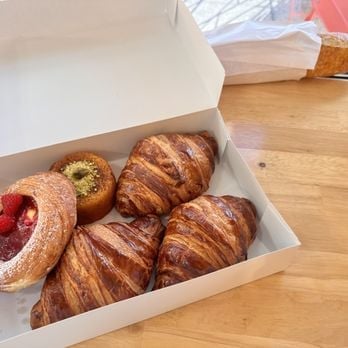 Open white pastry box containing croissants and filled pastries on wooden surface